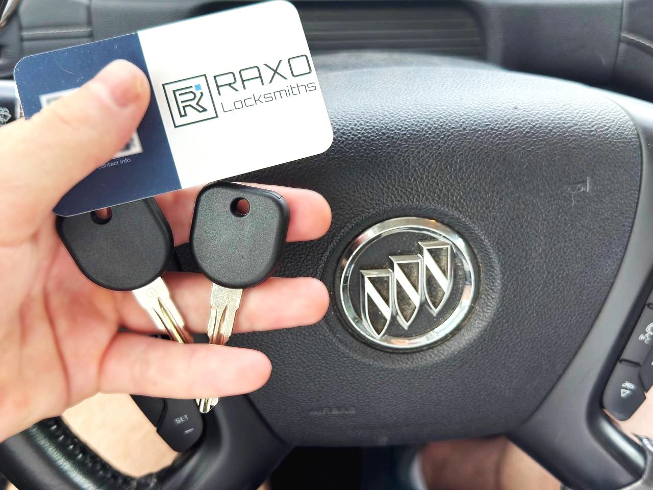 Two new transponder keys cut and programmed for a Buick after an all-keys-lost job in Winnipeg — Buick steering wheel behind