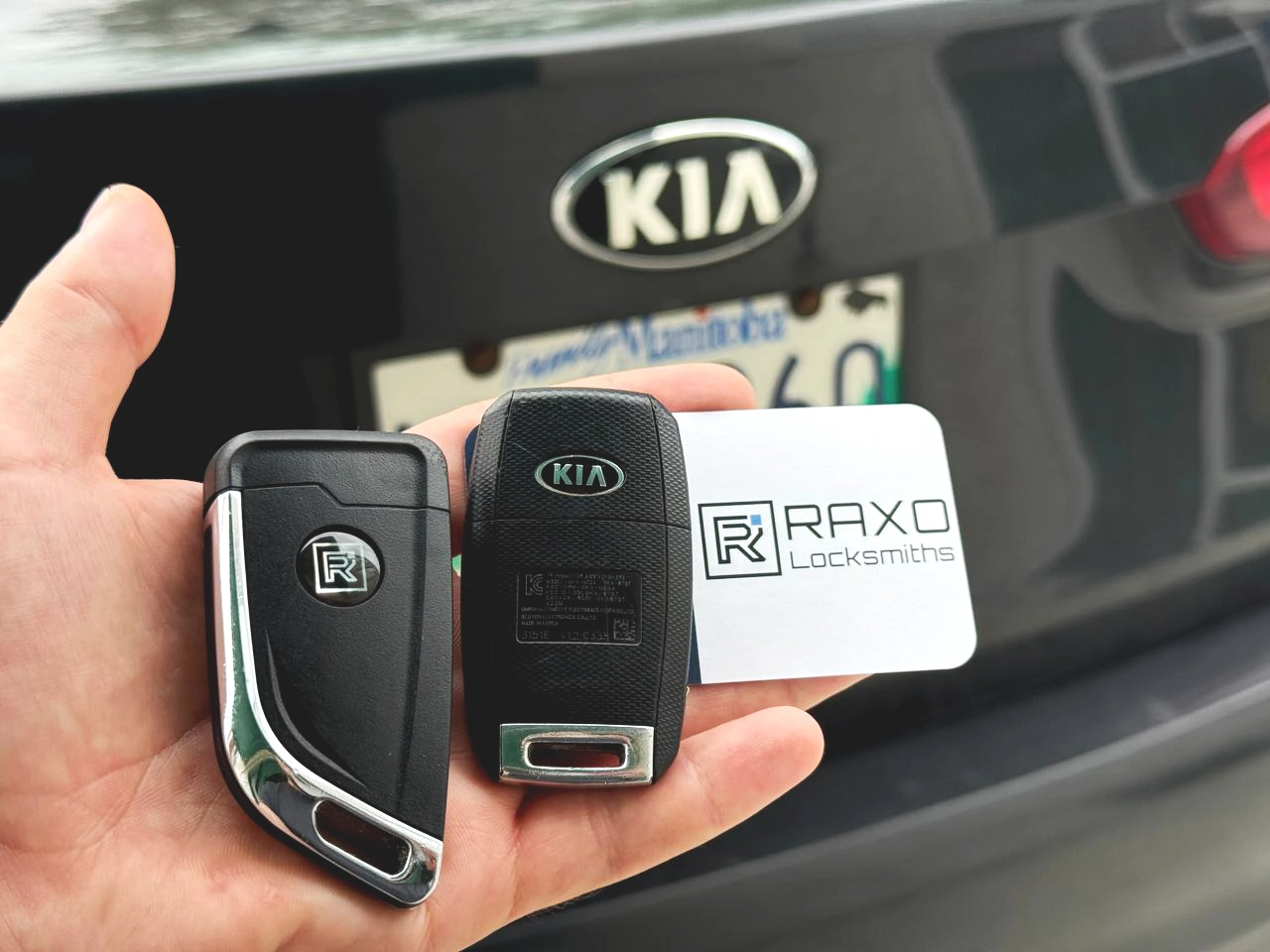 The same two Kia flip keys folded shut beside the Kia trunk badge — remote flip keys programmed on-site by RAXO Locksmiths