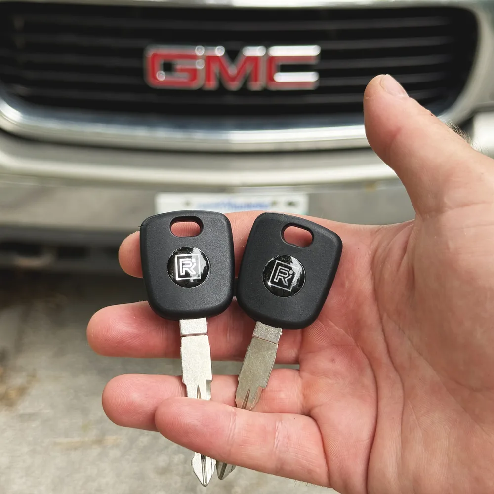 Two new GMC keys cut and programmed after an all-keys-lost job in Winnipeg, GMC grille behind