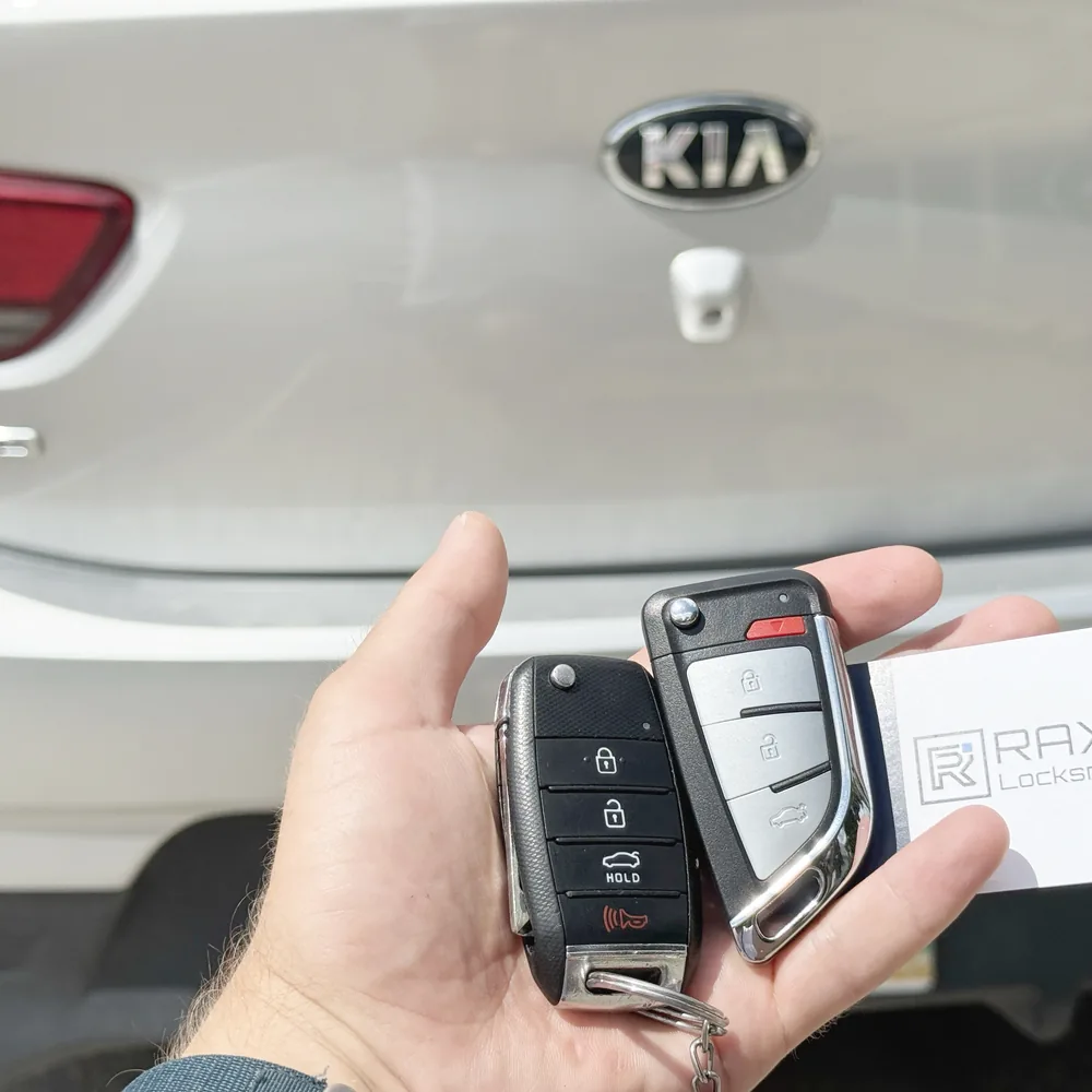 A new Kia Rio flip key cut and programmed beside the customer's key at a Kia in Winnipeg, RAXO card on the tailgate